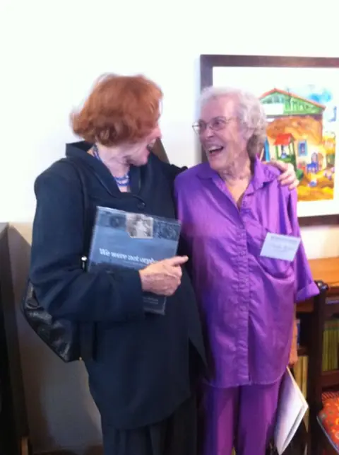 Two women laughing together, one holding a copy of the book
